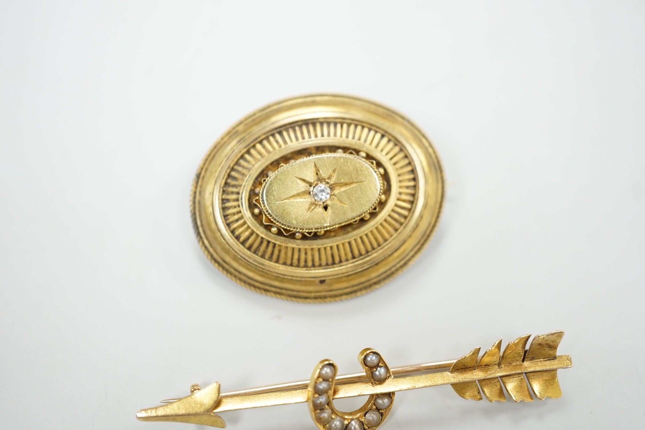 An early 20th century yellow metal, and seed pearl set arrow and horse shoe brooch, 60mm and a Victorian paste set yellow metal oval brooch.